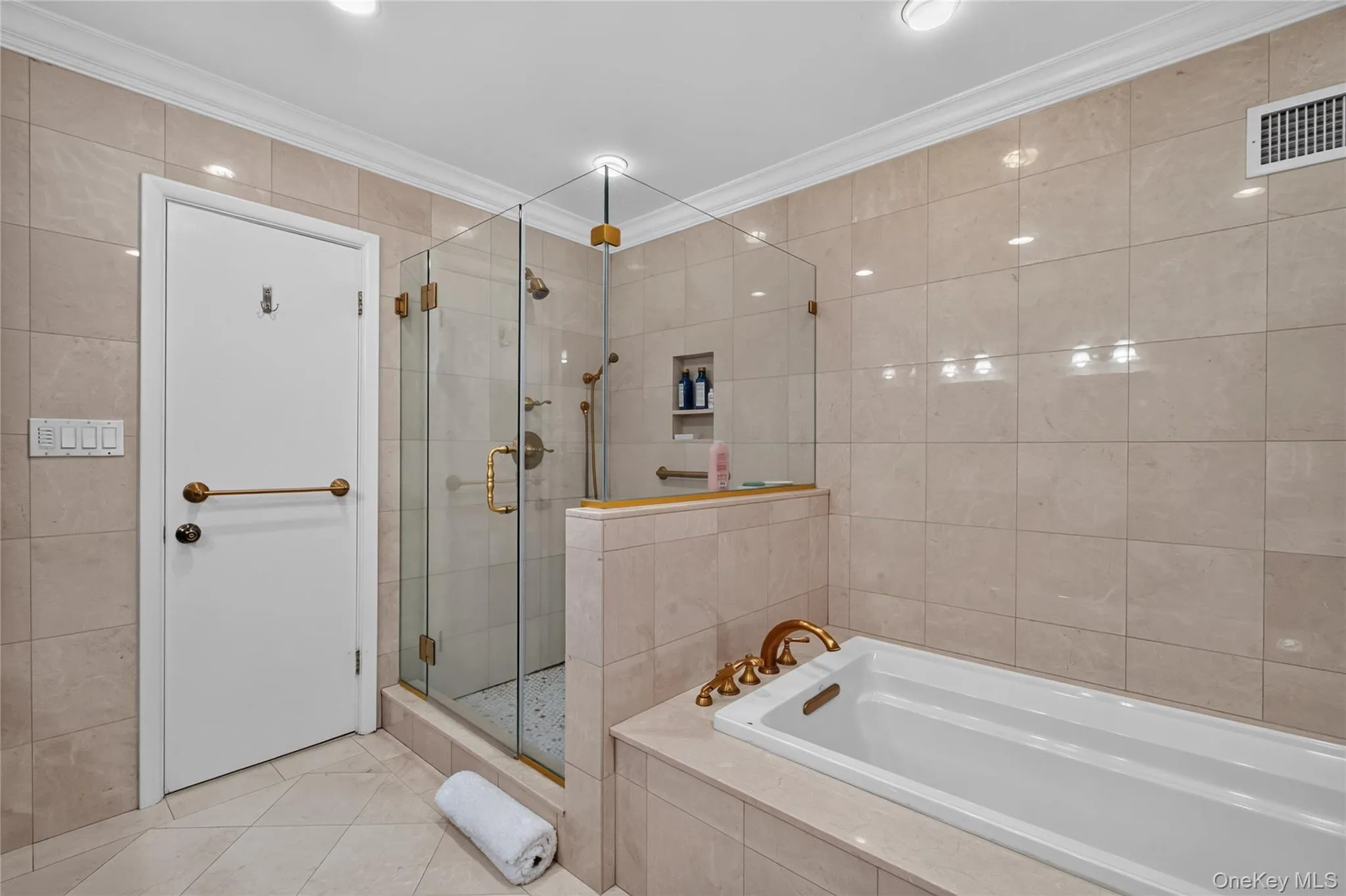 Bathroom featuring a built-in soaking tub with brass fixtures, a glass-enclosed shower with a tiled floor, and recessed shelving. Bathroom featuring a built-in soaking tub with brass fixtures, a glass-enclosed shower with a tiled floor, and recessed shelving.