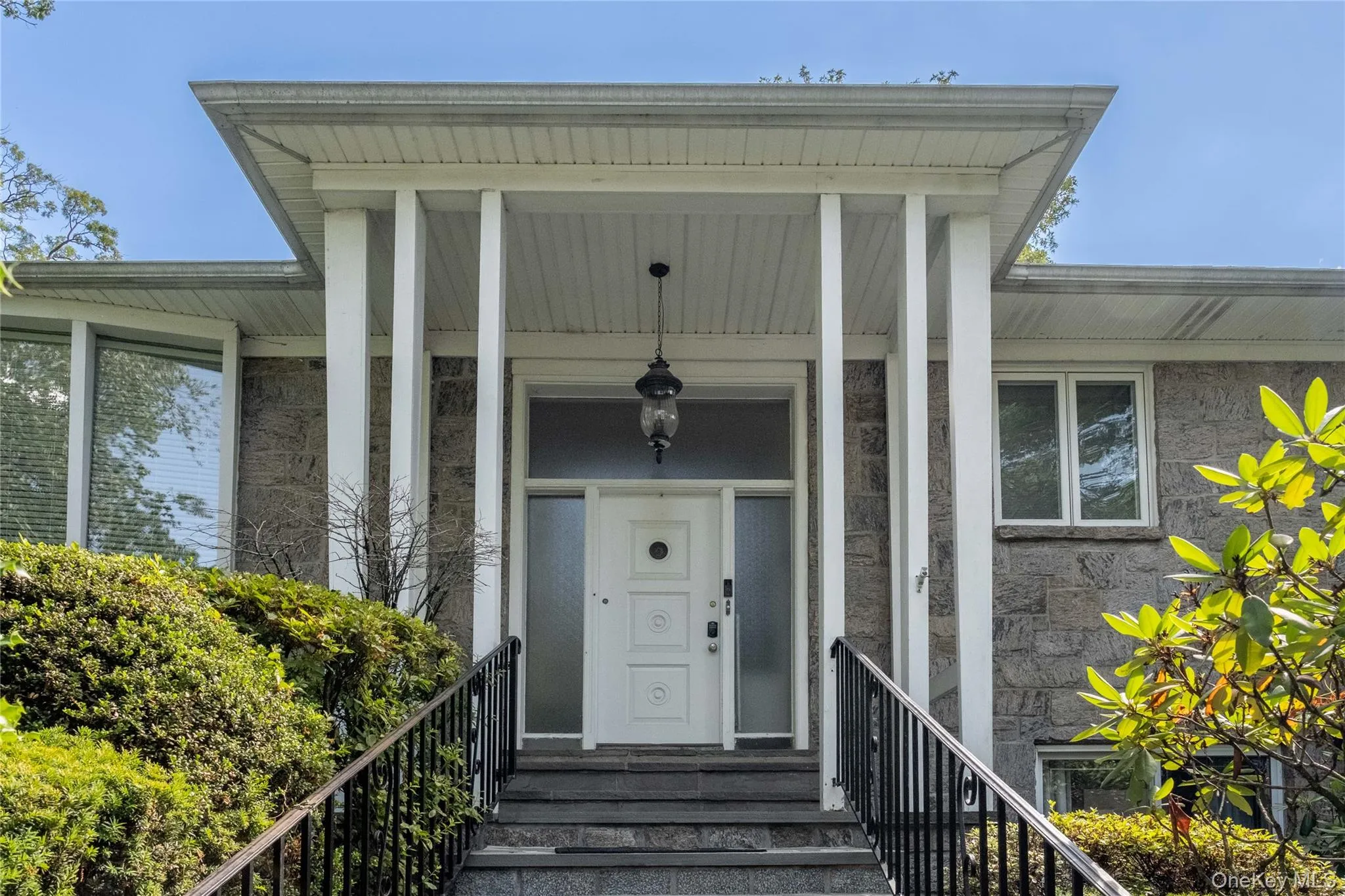 Stately entry featuring a white panel door with sidelights, an extended covered porch with recessed lighting, brand new black wrought iron railings, and blue stone steps. Stately entry featuring a white panel door with sidelights, an extended covered porch with recessed lighting, brand new black wrought iron railings, and blue stone steps.