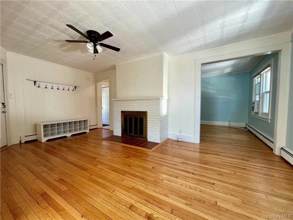 Living room with a decorative fireplace, ceiling fan, crown molding, hardwood floors, and baseboard heating Living room with a decorative fireplace, ceiling fan, crown molding, hardwood floors, and baseboard heating