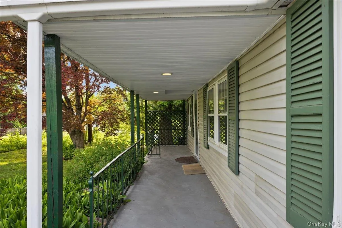 Covered front porch featuring a concrete surface, white vinyl siding, green louvered shutters, and recessed lighting Covered front porch featuring a concrete surface, white vinyl siding, green louvered shutters, and recessed lighting