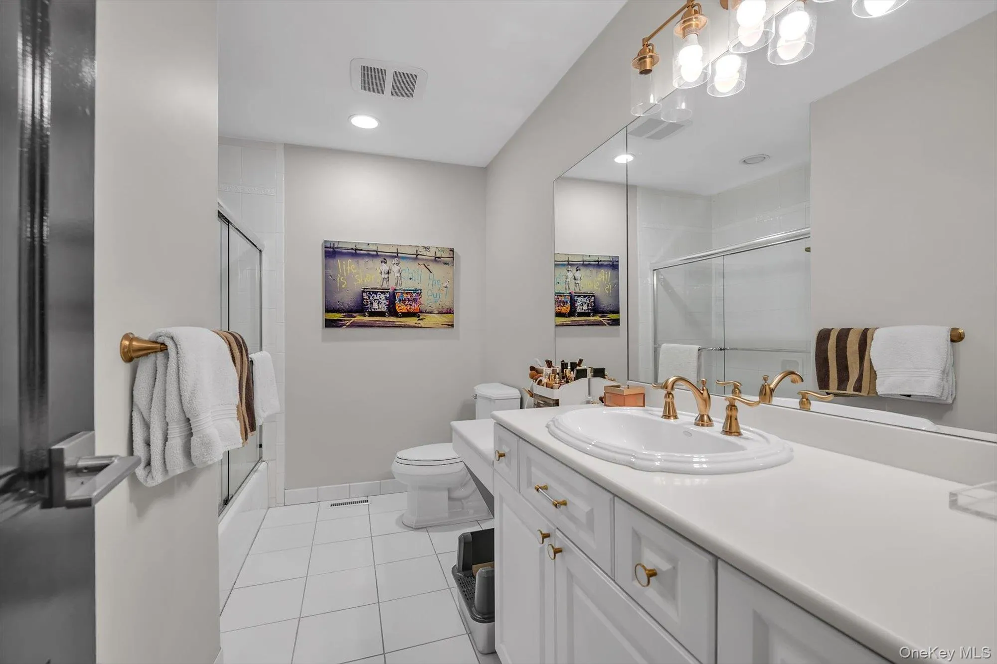 Bathroom featuring a white vanity with gold-tone fixtures, a built-in sink, and a large mirror Bathroom featuring a white vanity with gold-tone fixtures, a built-in sink, and a large mirror