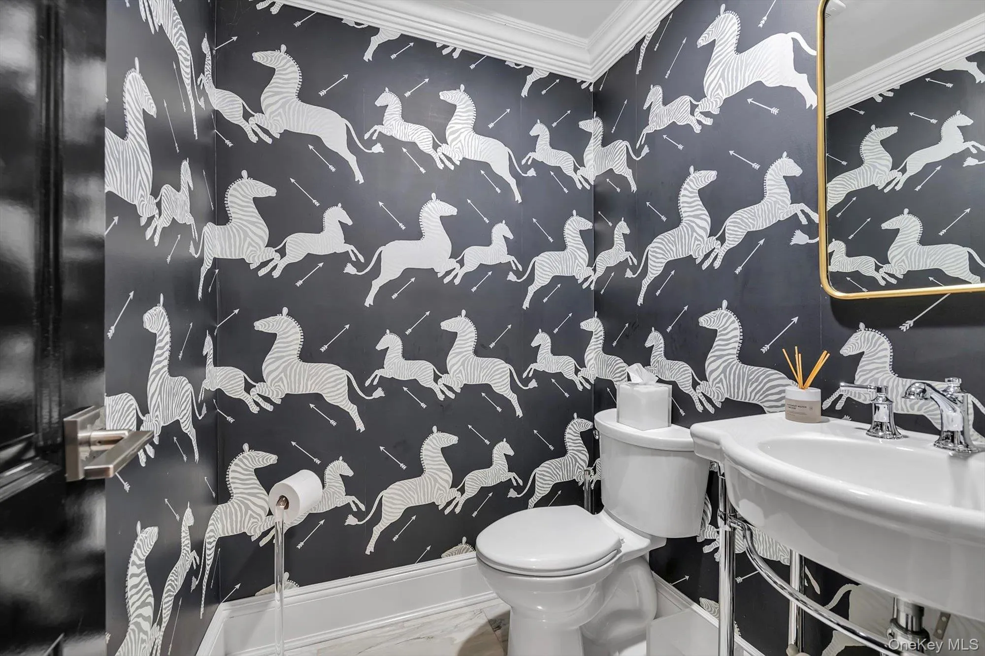 Powder room featuring whimsical patterned wallpaper, a classic white pedestal sink with chrome fixtures, and a polished gold-framed mirror. Powder room featuring whimsical patterned wallpaper, a classic white pedestal sink with chrome fixtures, and a polished gold-framed mirror.