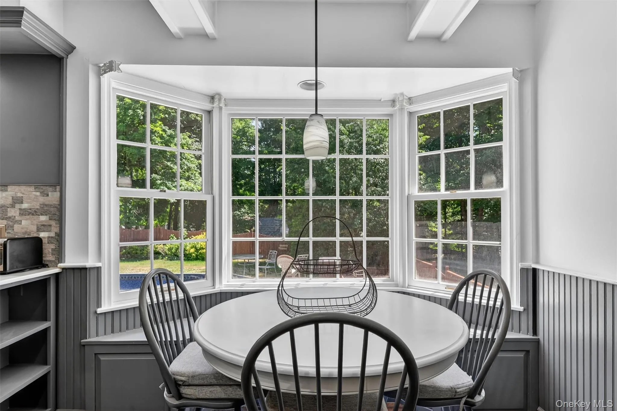 Bay window with multiple paneled windows, beadboard wainscoting, built-in bench seating, coffered ceiling detail, and a modern pendant light fixture Bay window with multiple paneled windows, beadboard wainscoting, built-in bench seating, coffered ceiling detail, and a modern pendant light fixture