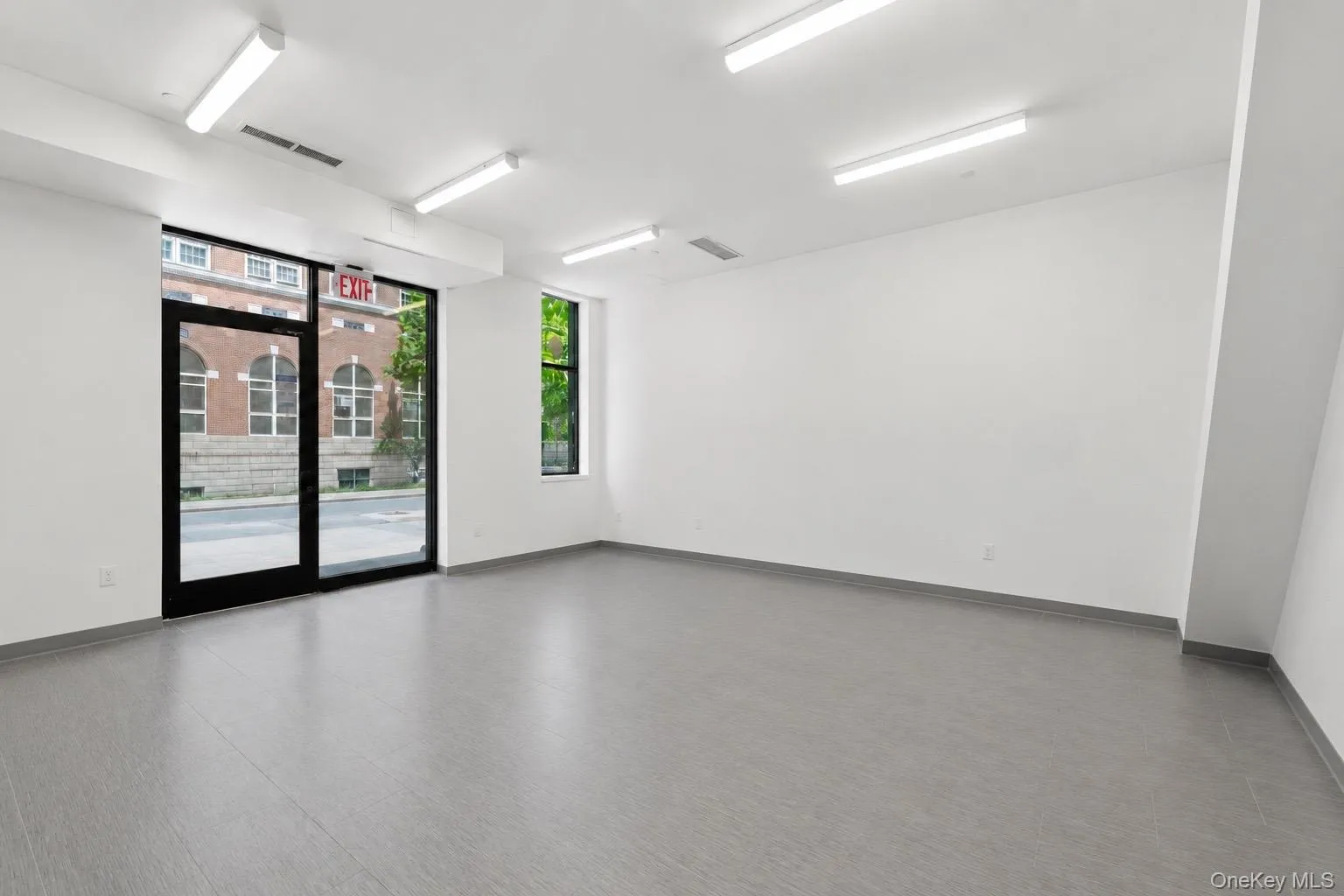 Spacious commercial interior featuring full-height storefront glass, a separate large window, recessed fluorescent lighting, light gray wood-finish flooring, and white walls Spacious commercial interior featuring full-height storefront glass, a separate large window, recessed fluorescent lighting, light gray wood-finish flooring, and white walls
