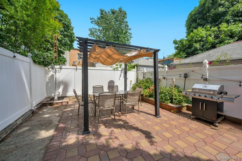 Paved patio featuring a black pergola with a retractable fabric canopy, bordered by a built-in planter box Paved patio featuring a black pergola with a retractable fabric canopy, bordered by a built-in planter box