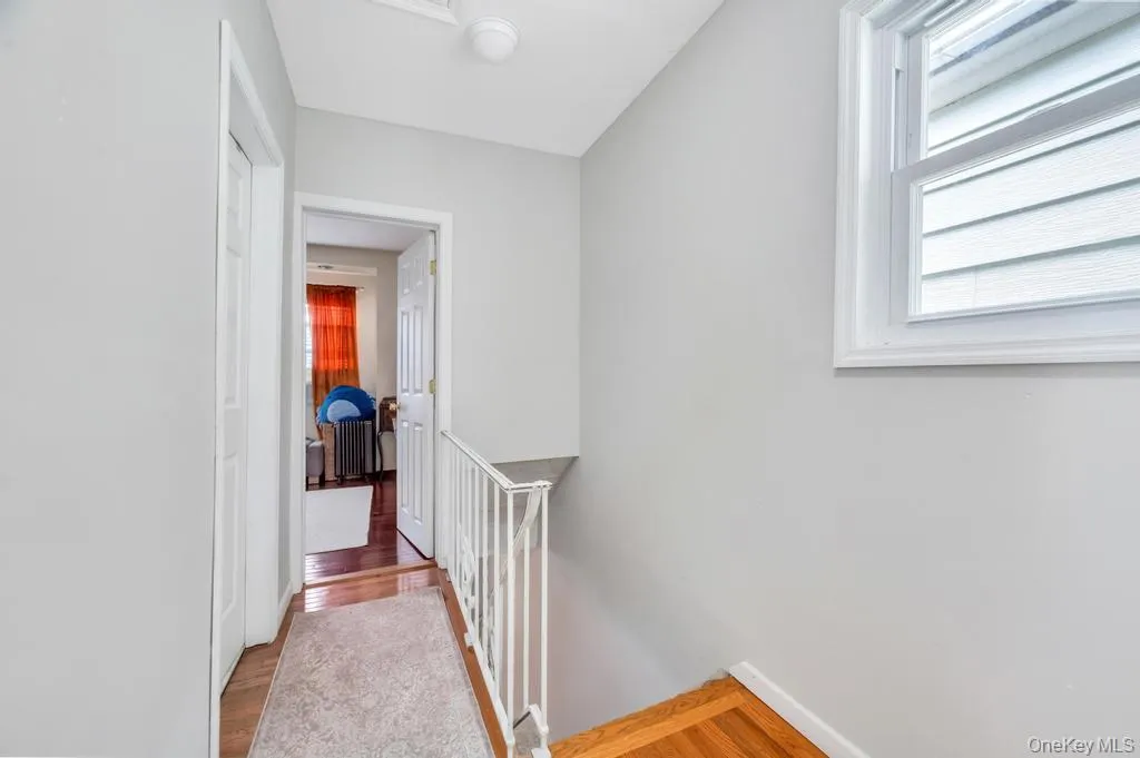 Hallway featuring light gray walls, wood-finish flooring, white trim, and a white painted banister Hallway featuring light gray walls, wood-finish flooring, white trim, and a white painted banister