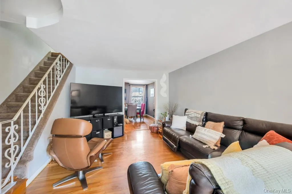 Living area featuring wood-finish flooring, a neutral wall color, and a carpeted staircase with decorative white railings Living area featuring wood-finish flooring, a neutral wall color, and a carpeted staircase with decorative white railings