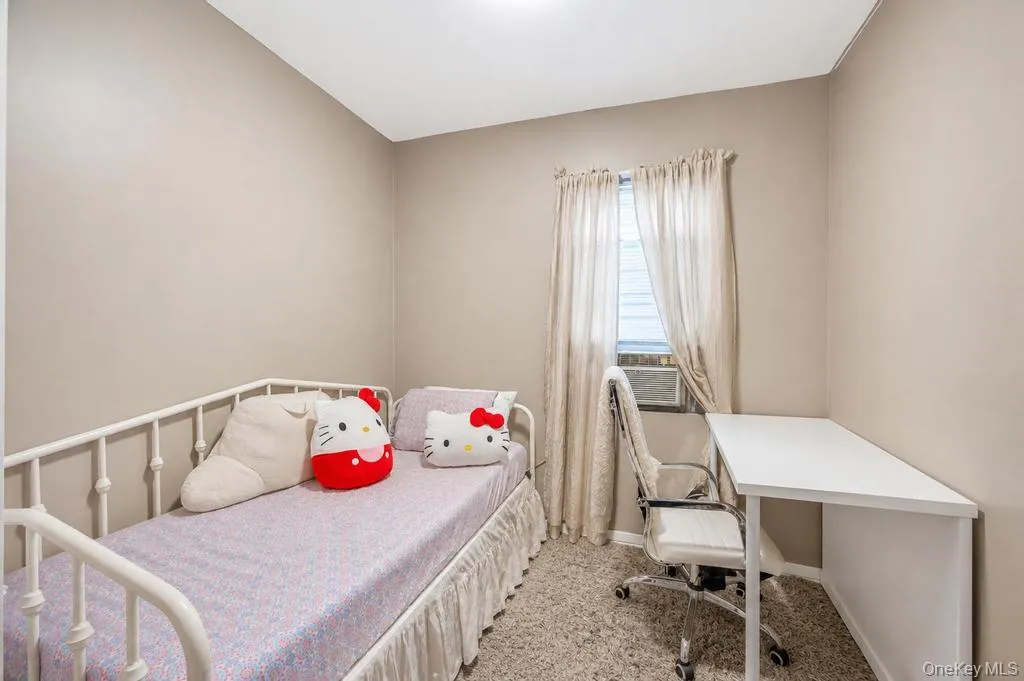 Bedroom featuring neutral wall paint, carpet flooring, a window with sheer curtains, and a built-in air conditioning unit Bedroom featuring neutral wall paint, carpet flooring, a window with sheer curtains, and a built-in air conditioning unit