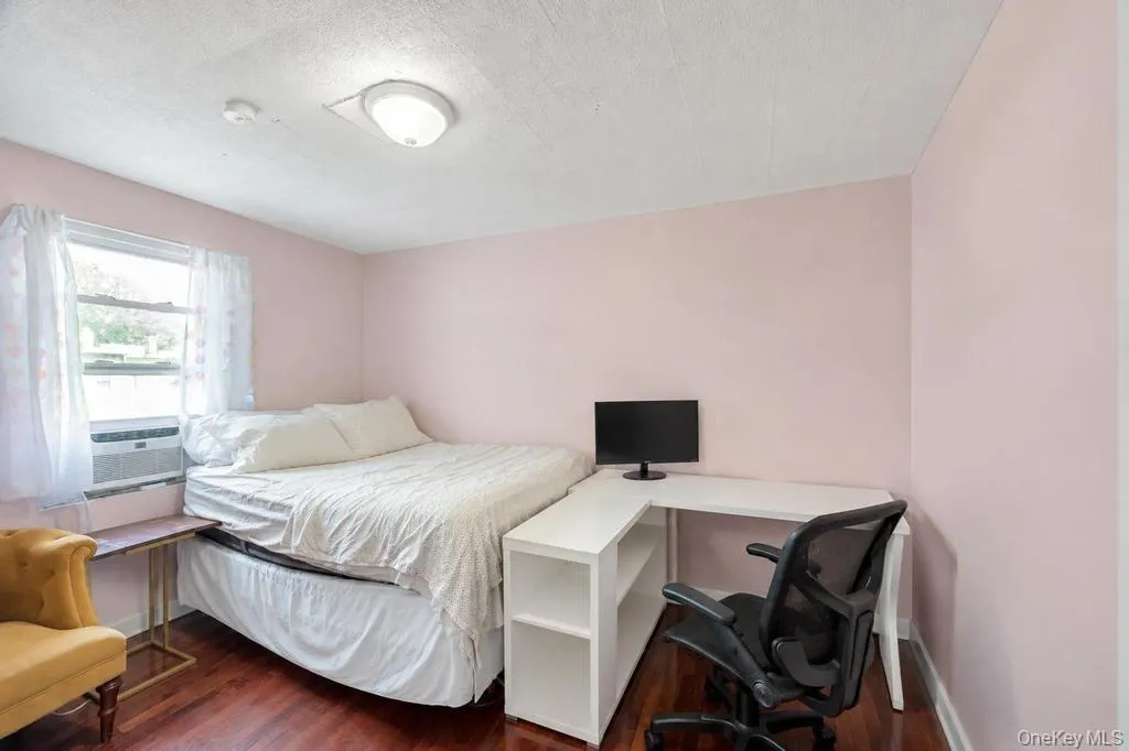 Bedroom featuring a window-mounted air conditioning unit, wood-finish flooring, and a flush-mount ceiling light fixture Bedroom featuring a window-mounted air conditioning unit, wood-finish flooring, and a flush-mount ceiling light fixture