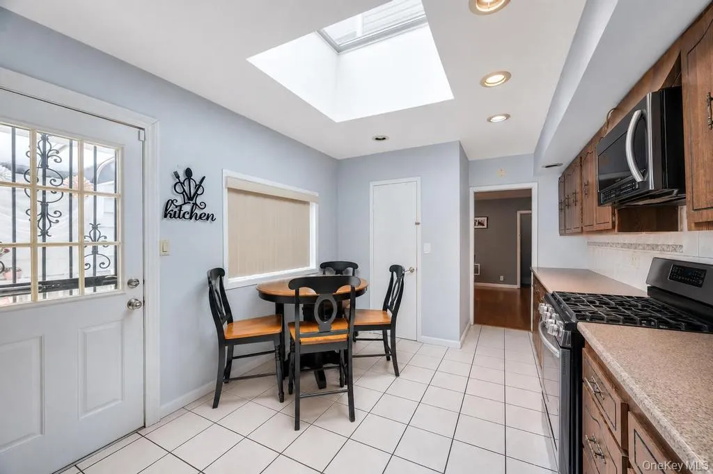 Kitchen featuring white tile flooring, wooden cabinetry, stainless steel oven, recessed lighting, and a skylight Kitchen featuring white tile flooring, wooden cabinetry, stainless steel oven, recessed lighting, and a skylight