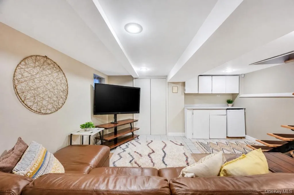 Recessed lighting illuminates this versatile lower-level space, featuring a built-in wet bar with white cabinetry and a compact refrigerator Recessed lighting illuminates this versatile lower-level space, featuring a built-in wet bar with white cabinetry and a compact refrigerator