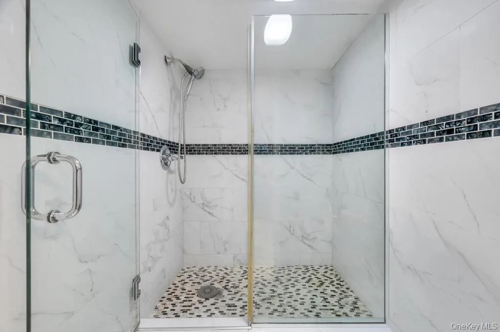 Glass-enclosed shower featuring white wall tiling with dark accent band, pebble-style floor tiling, and chrome fixtures Glass-enclosed shower featuring white wall tiling with dark accent band, pebble-style floor tiling, and chrome fixtures