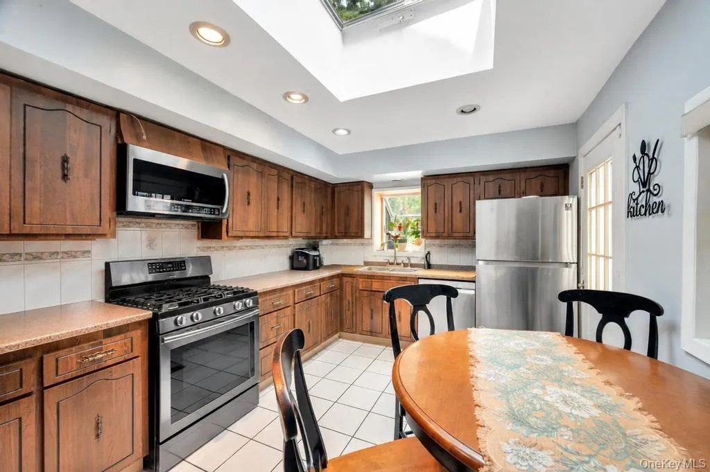 Kitchen featuring abundant wood cabinetry, recessed lighting, a skylight, stainless steel appliances, and tile flooring Kitchen featuring abundant wood cabinetry, recessed lighting, a skylight, stainless steel appliances, and tile flooring