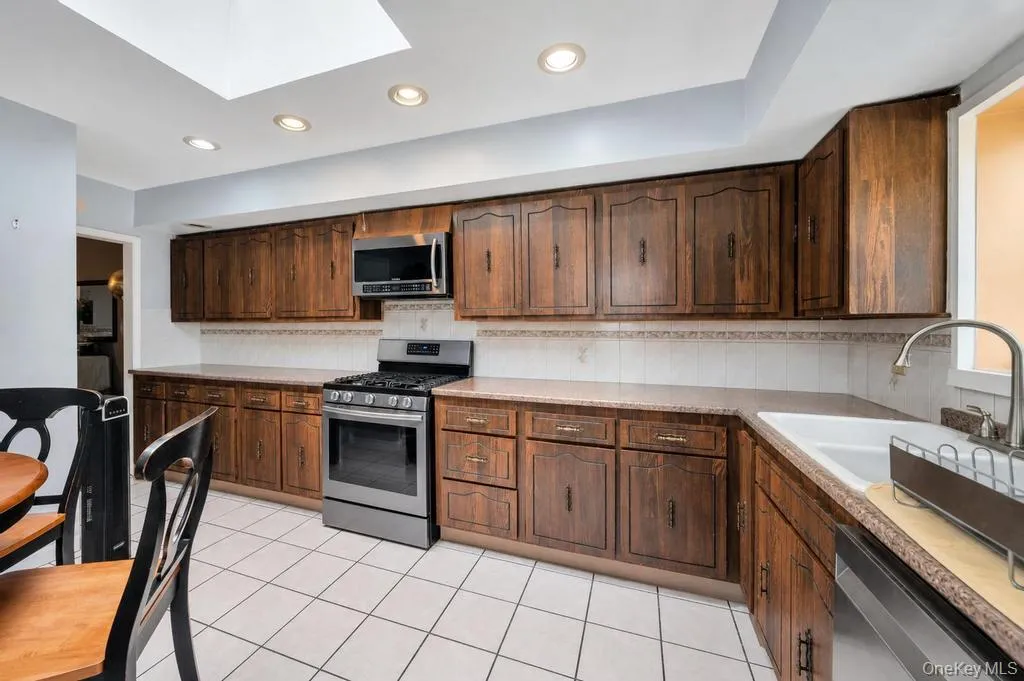 Kitchen featuring wood-finish cabinetry, tile flooring, and light countertops Kitchen featuring wood-finish cabinetry, tile flooring, and light countertops