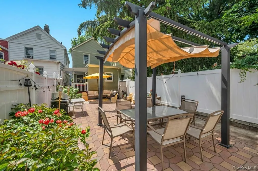 Paved patio featuring a pergola with a retractable fabric shade, surrounded by lush landscaping and privacy fencing Paved patio featuring a pergola with a retractable fabric shade, surrounded by lush landscaping and privacy fencing