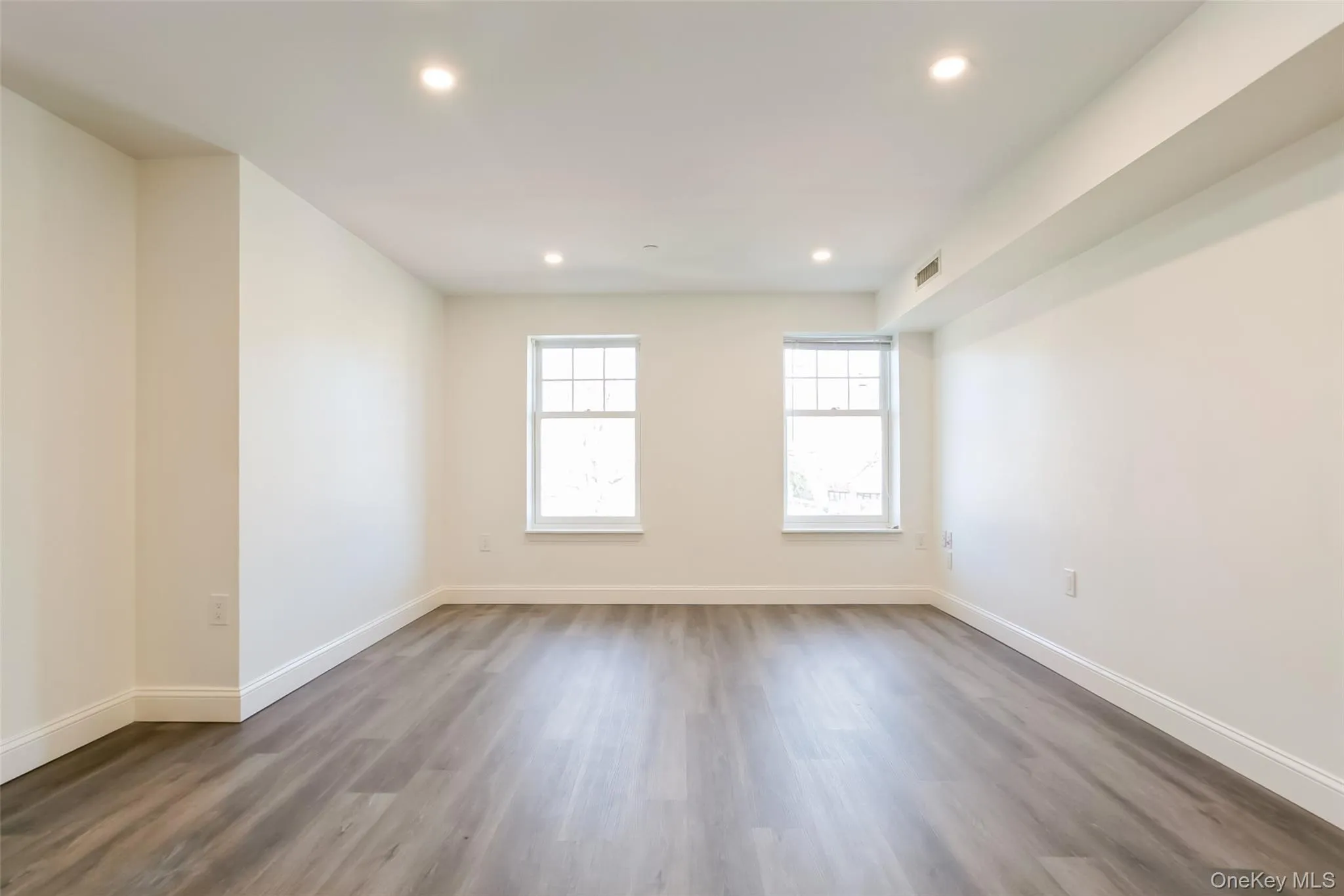 Empty room featuring recessed lighting, visible vents, baseboards, and dark wood-style floors Empty room featuring recessed lighting, visible vents, baseboards, and dark wood-style floors