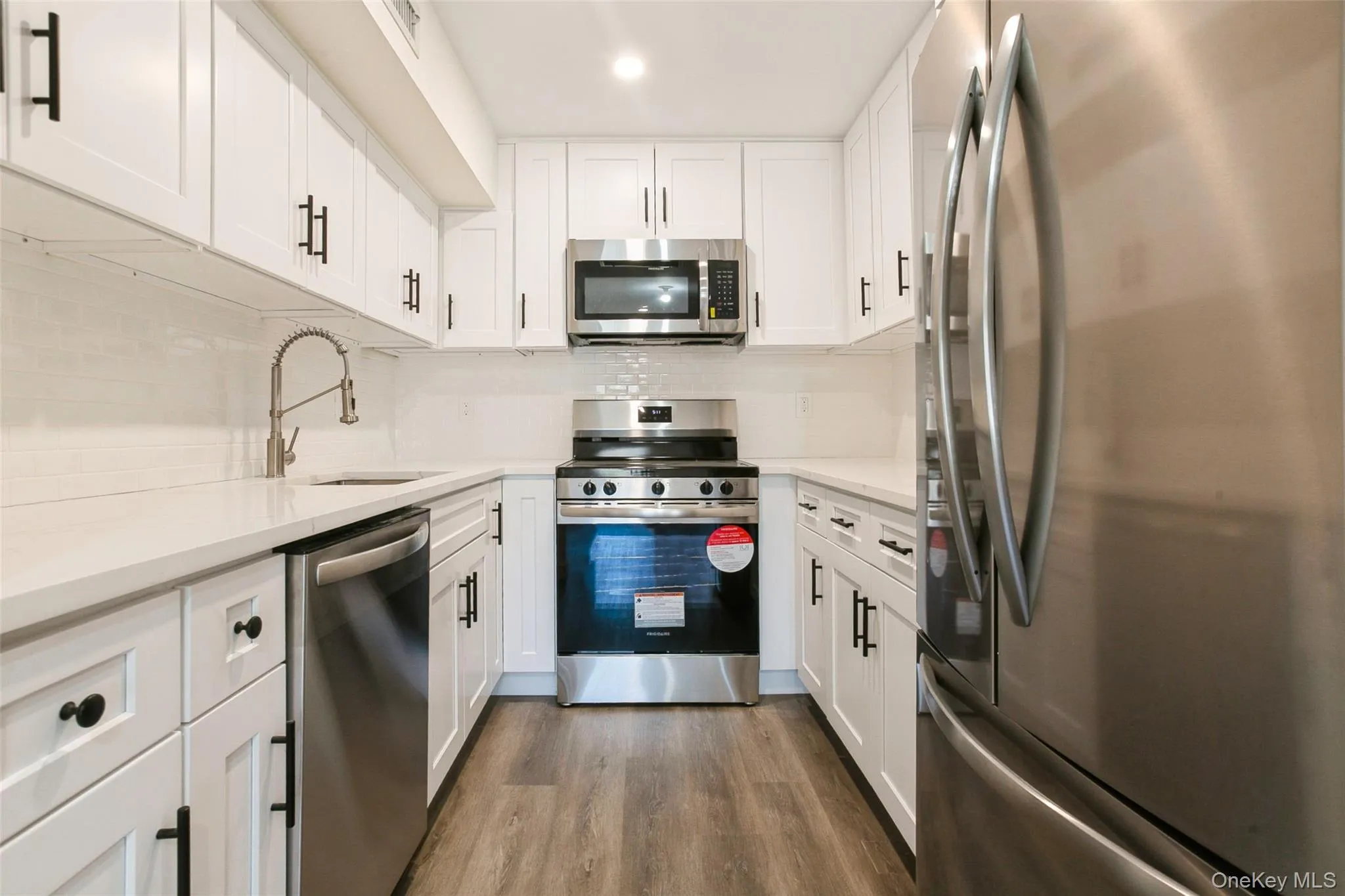 Kitchen with backsplash, dark wood finished floors, stainless steel appliances, white cabinetry, and a sink Kitchen with backsplash, dark wood finished floors, stainless steel appliances, white cabinetry, and a sink