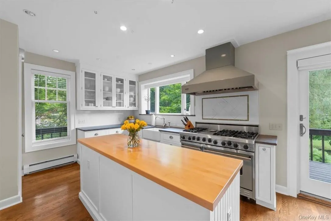 Kitchen featuring range with two ovens, backsplash, light wood-type flooring, baseboard heating, and wall chimney exhaust hood Kitchen featuring range with two ovens, backsplash, light wood-type flooring, baseboard heating, and wall chimney exhaust hood