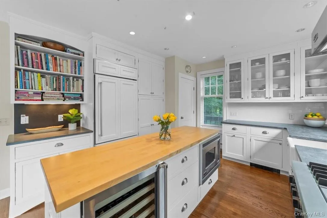 Kitchen with white cabinetry, stainless steel microwave, beverage cooler, backsplash, and dark wood-type flooring Kitchen with white cabinetry, stainless steel microwave, beverage cooler, backsplash, and dark wood-type flooring