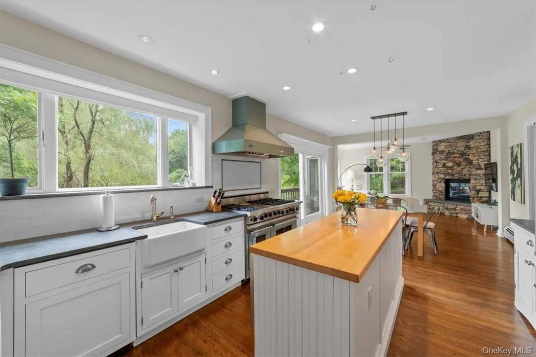 Kitchen featuring wall chimney range hood, dark hardwood / wood-style floors, range with two ovens, decorative backsplash, and a stone fireplace Kitchen featuring wall chimney range hood, dark hardwood / wood-style floors, range with two ovens, decorative backsplash, and a stone fireplace