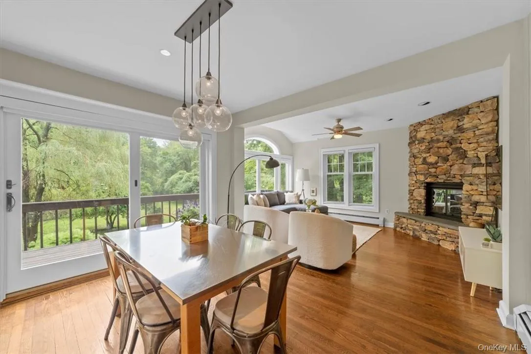 Dining space with hardwood / wood-style flooring, a baseboard heating unit, ceiling fan with notable chandelier, and a stone fireplace Dining space with hardwood / wood-style flooring, a baseboard heating unit, ceiling fan with notable chandelier, and a stone fireplace