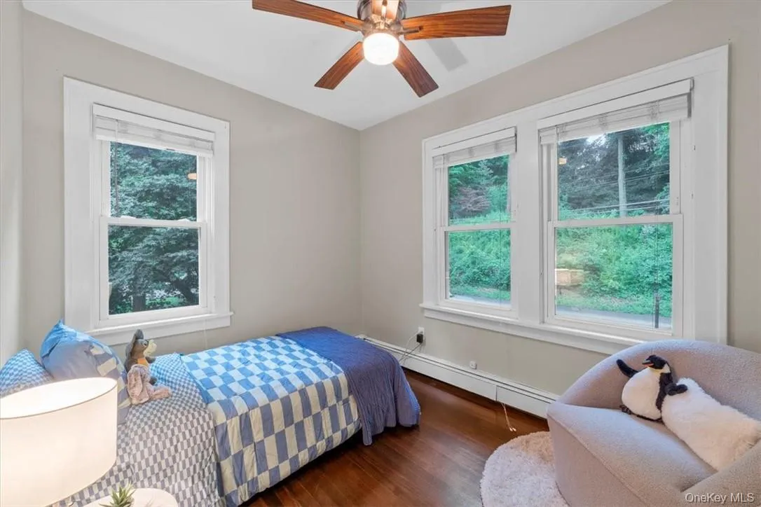 Bedroom with ceiling fan, multiple windows, dark hardwood / wood-style floors, and baseboard heating Bedroom with ceiling fan, multiple windows, dark hardwood / wood-style floors, and baseboard heating