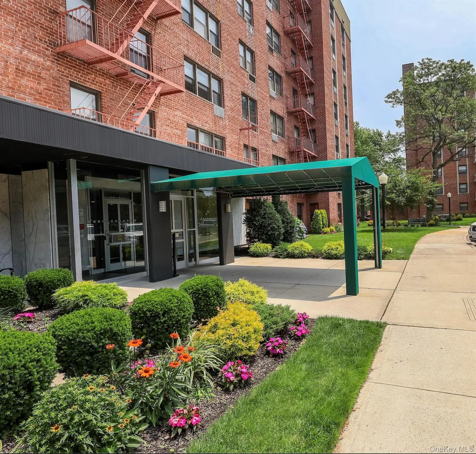 Brick facade building featuring a covered entryway, mature landscaping, manicured lawn, and paved walkways Brick facade building featuring a covered entryway, mature landscaping, manicured lawn, and paved walkways