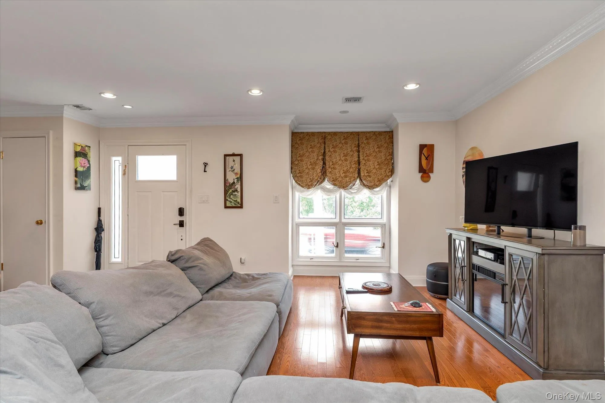 Sunny living room featuring wood-finish flooring, and a window with patterned Roman shades Sunny living room featuring wood-finish flooring, and a window with patterned Roman shades