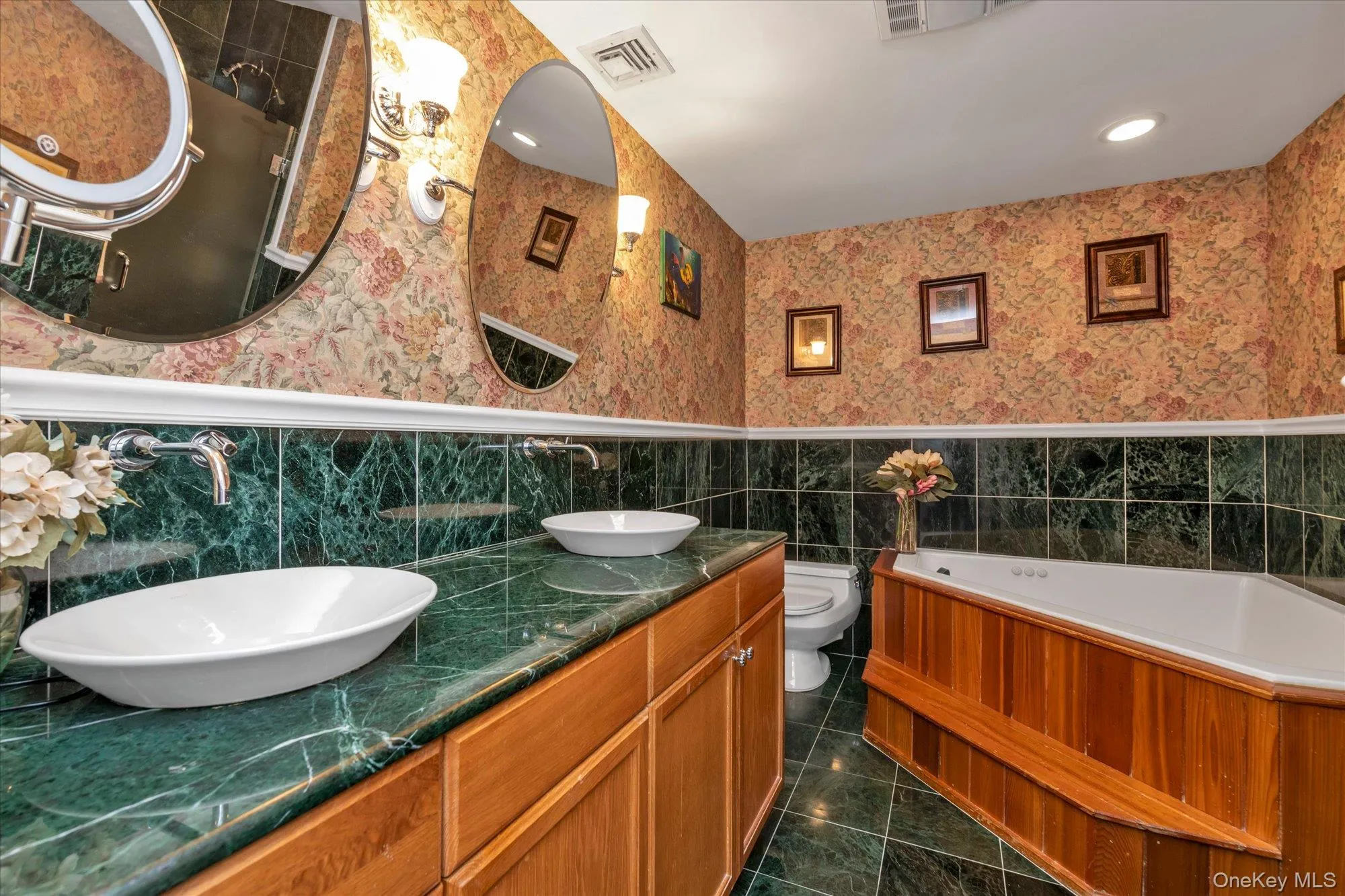 Ensuite master bathroom featuring a jetted tub with a wood-paneled surround, full shower area, dual vessel sinks, a green marble-finish countertop. Ensuite master bathroom featuring a jetted tub with a wood-paneled surround, full shower area, dual vessel sinks, a green marble-finish countertop.