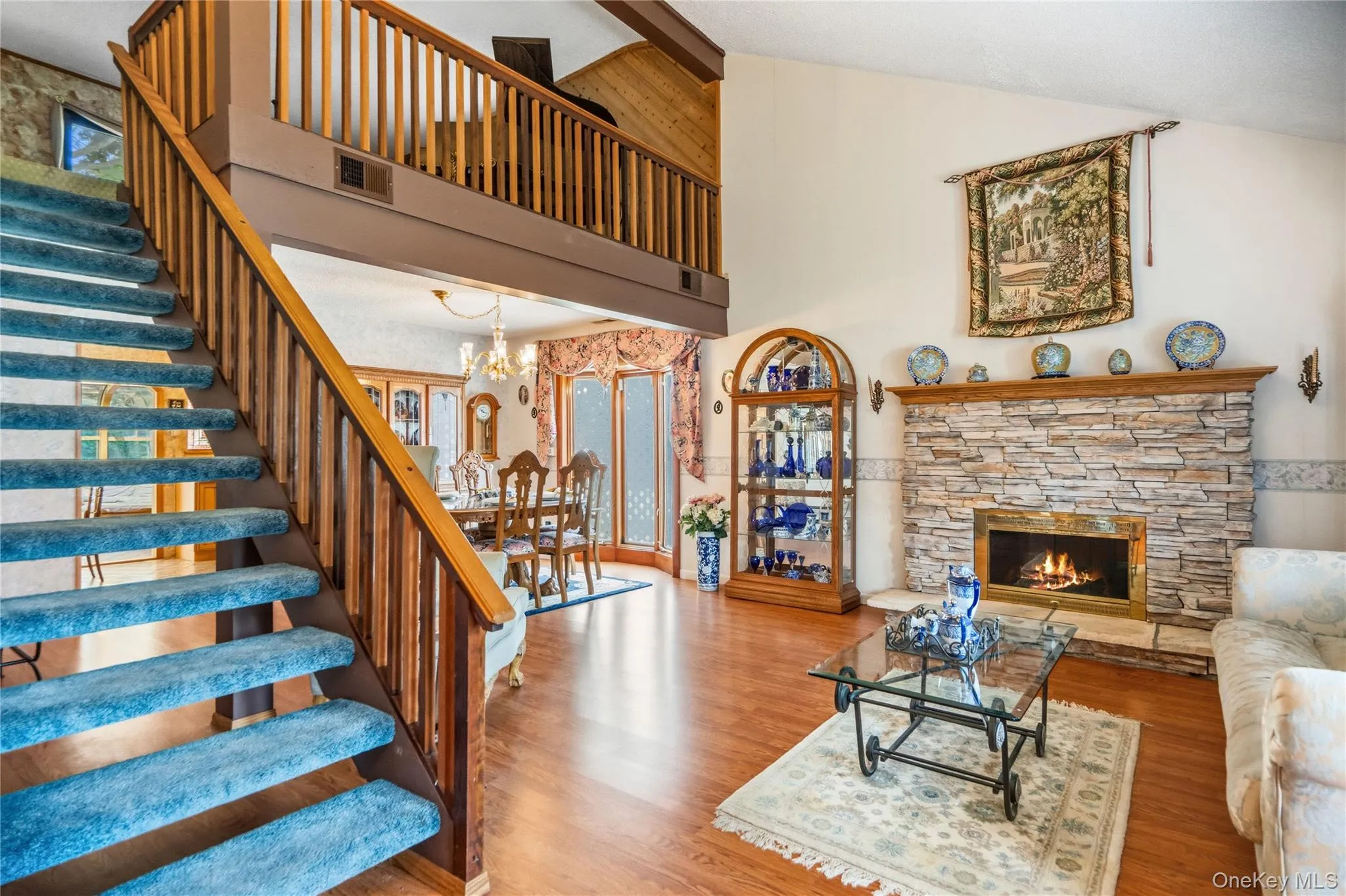 Open-concept living area featuring wood-finish, vinyl flooring, a two-story vaulted ceiling and a prominent staircase with wood railings leading to the lofted family room. Open-concept living area featuring wood-finish, vinyl flooring, a two-story vaulted ceiling and a prominent staircase with wood railings leading to the lofted family room.
