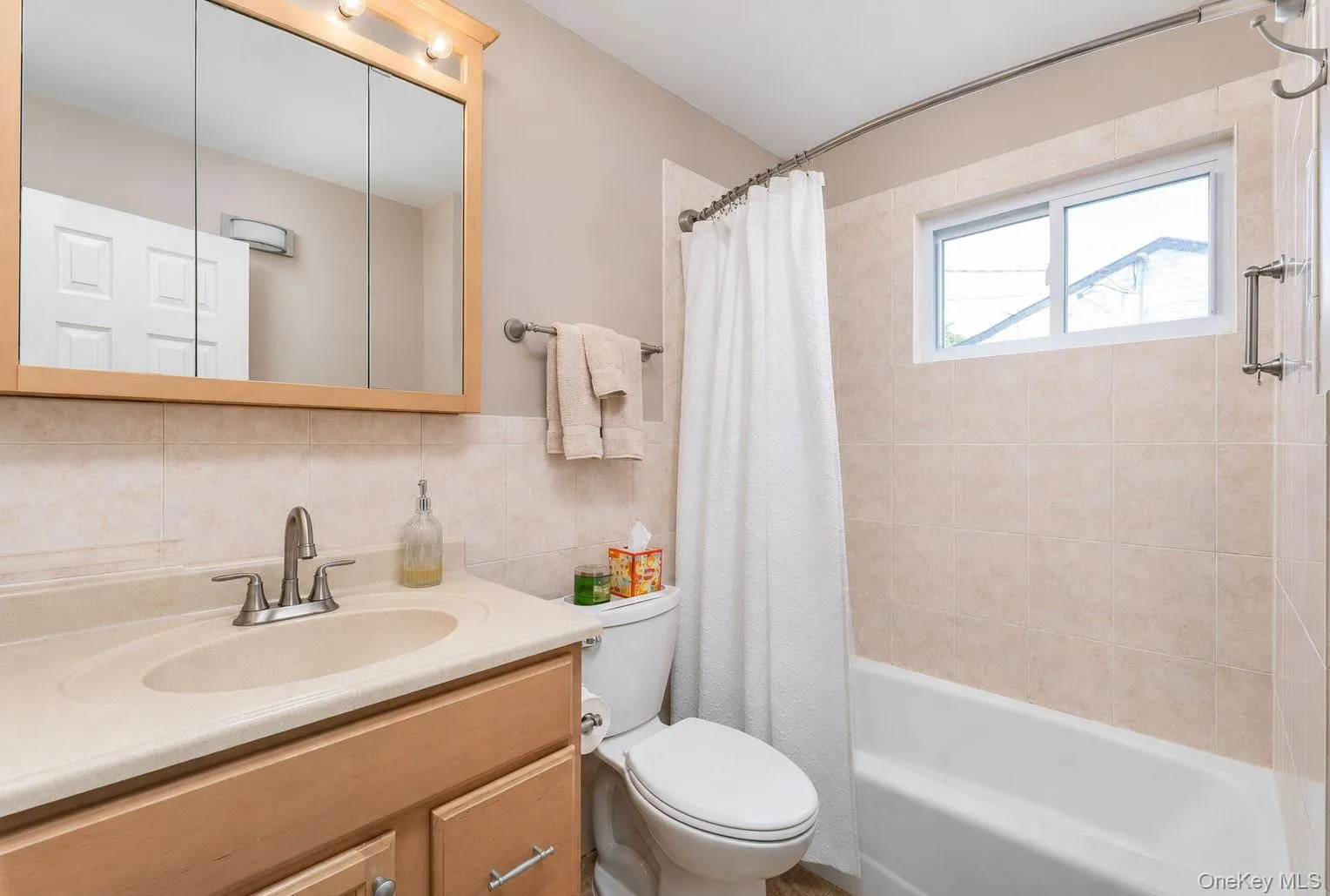 Bathroom featuring a light wood-finish vanity with an integrated sink, polished chrome faucet, and a large mirrored medicine cabinet with overhead lighting Bathroom featuring a light wood-finish vanity with an integrated sink, polished chrome faucet, and a large mirrored medicine cabinet with overhead lighting