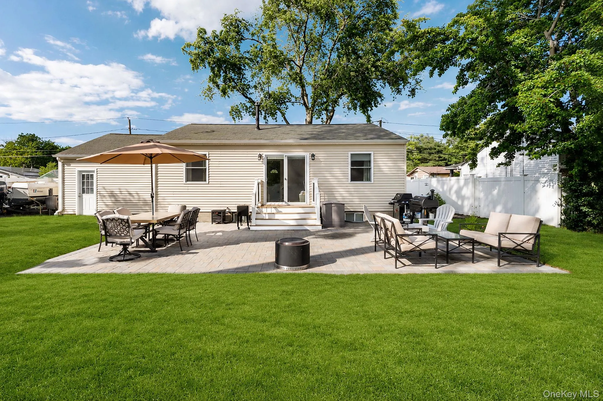 Expansive backyard featuring a paver patio with direct access to the interior via sliding glass doors, a side entry door, and a white privacy fence along the property line Expansive backyard featuring a paver patio with direct access to the interior via sliding glass doors, a side entry door, and a white privacy fence along the property line