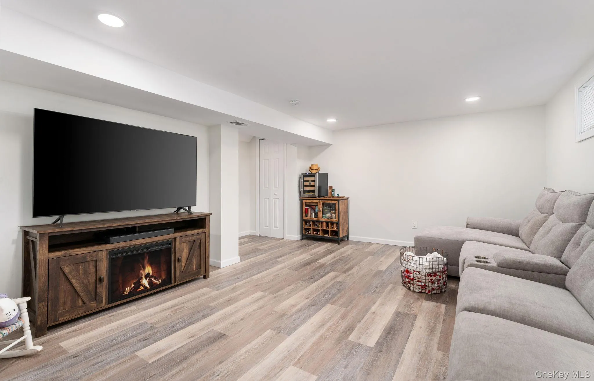 Finished basement room featuring recessed lighting, wood-finish flooring, and a media console with an electric fireplace insert Finished basement room featuring recessed lighting, wood-finish flooring, and a media console with an electric fireplace insert