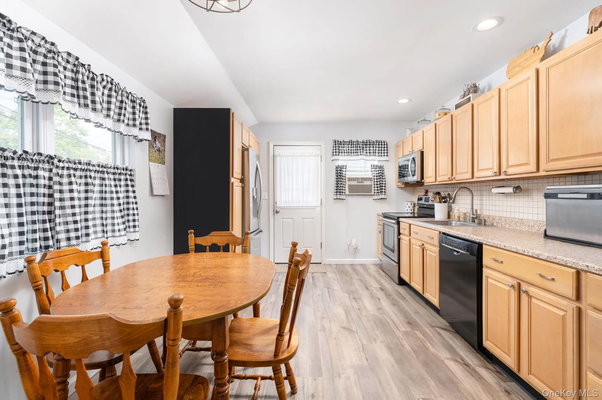 Kitchen featuring wood-finish flooring, light wood cabinetry, tile backsplash, and light-colored countertops Kitchen featuring wood-finish flooring, light wood cabinetry, tile backsplash, and light-colored countertops