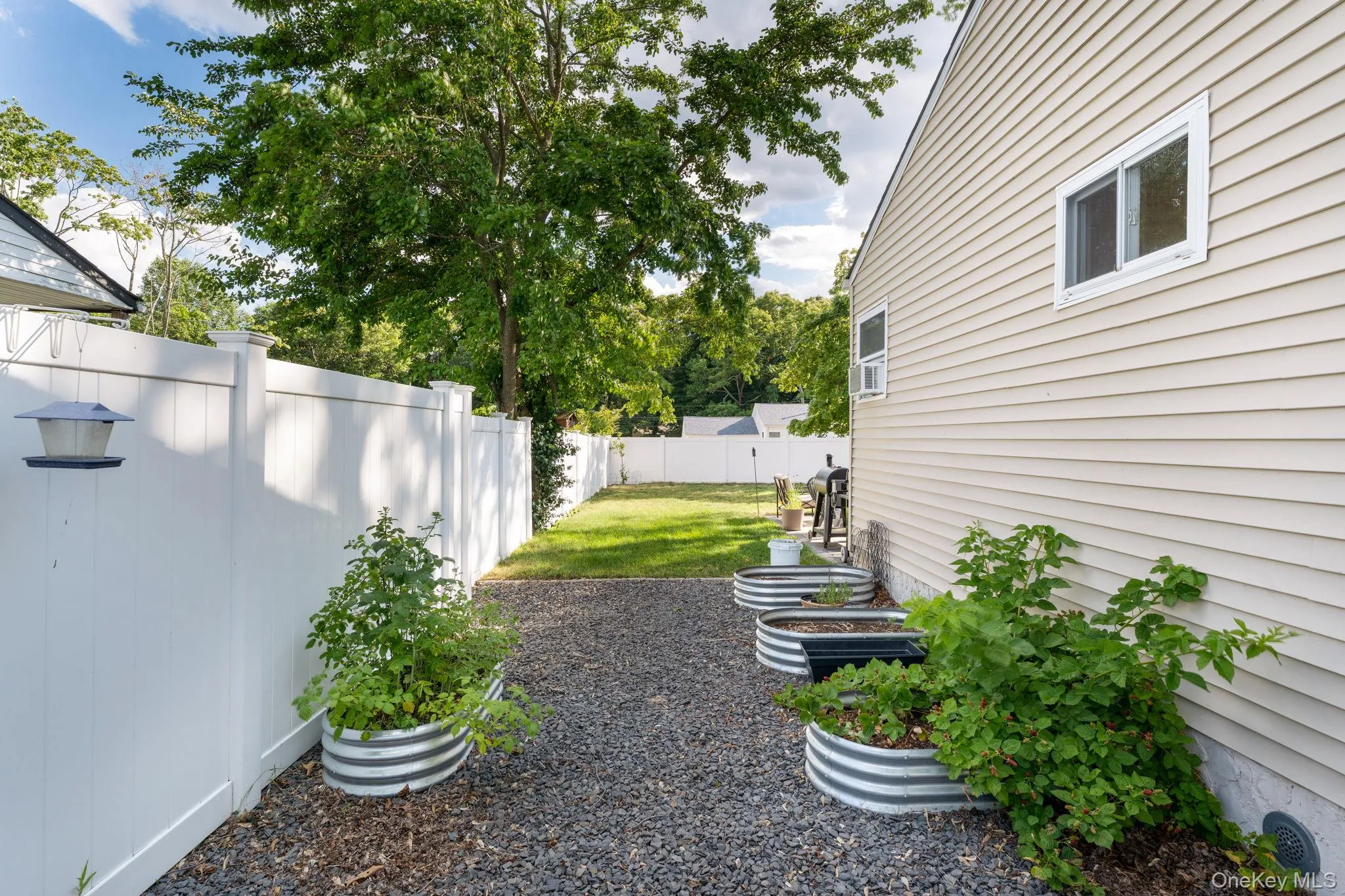 Side yard featuring gravel ground cover, raised garden beds, and a white privacy fence Side yard featuring gravel ground cover, raised garden beds, and a white privacy fence