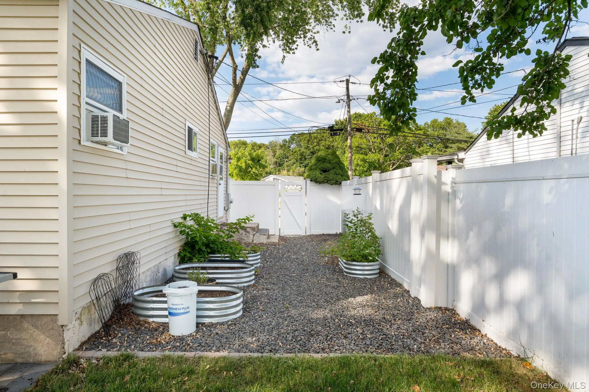 Side yard with gravel ground cover, multiple raised garden beds, and a white privacy fence Side yard with gravel ground cover, multiple raised garden beds, and a white privacy fence
