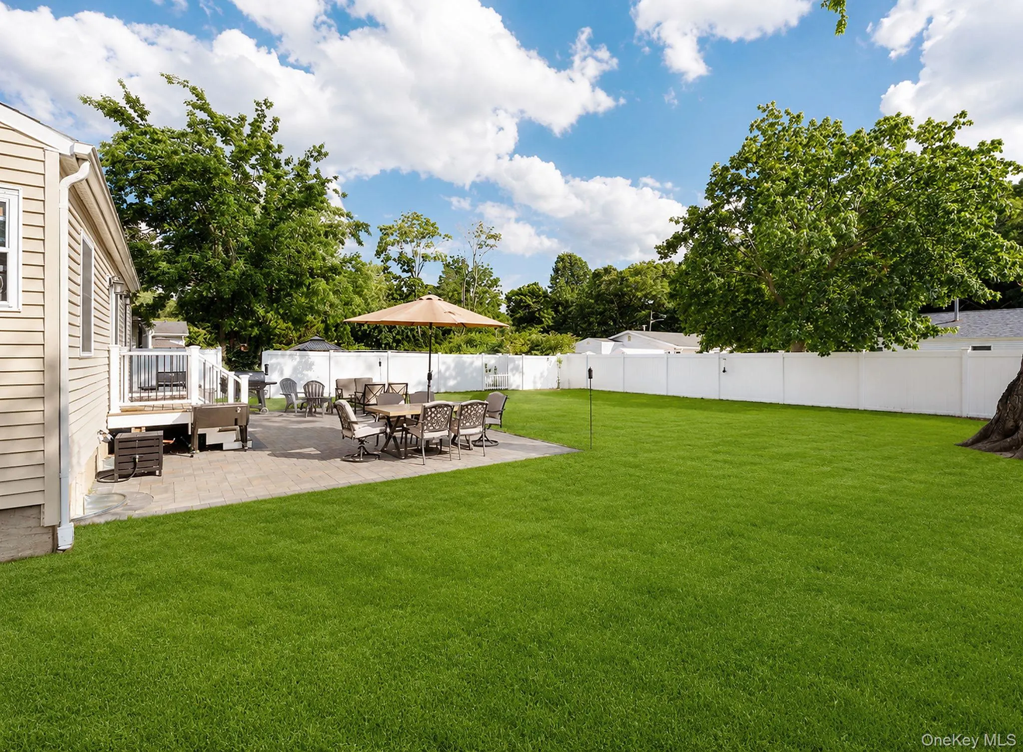 Expansive backyard featuring a lush lawn, white privacy fencing, and mature trees Expansive backyard featuring a lush lawn, white privacy fencing, and mature trees