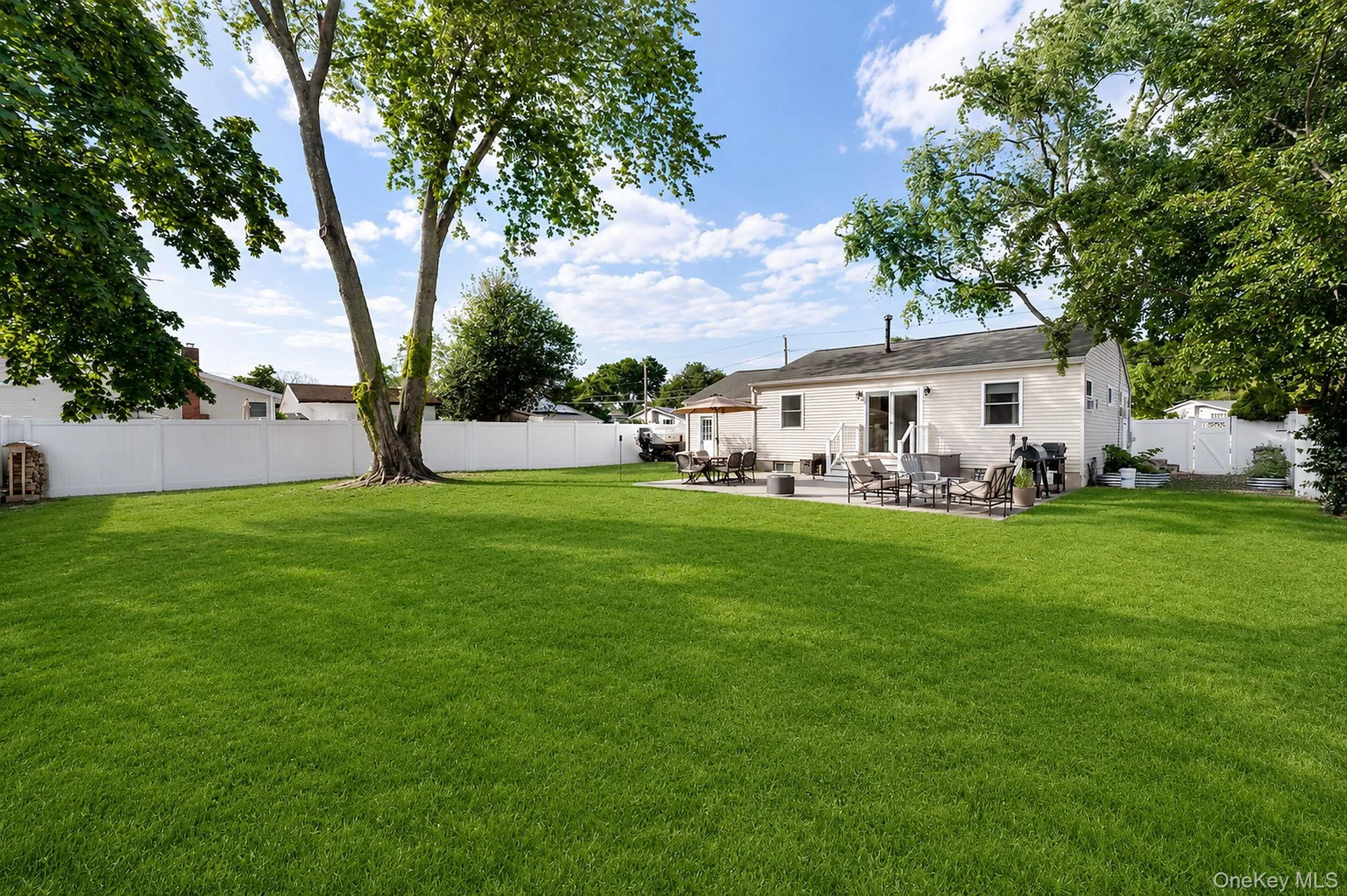 Spacious backyard with a large lawn, mature trees, a white privacy fence, and a paver patio. Spacious backyard with a large lawn, mature trees, a white privacy fence, and a paver patio.
