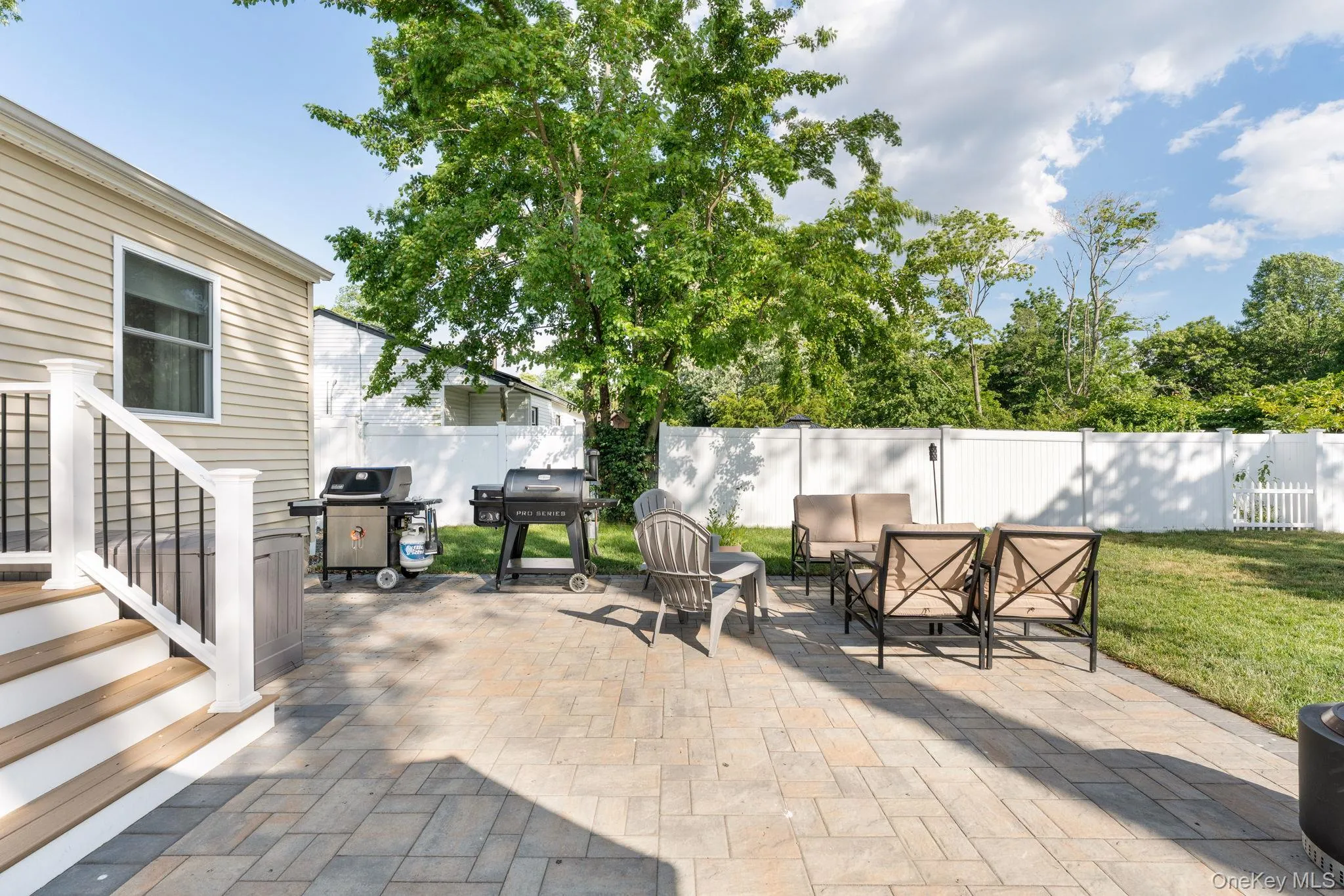 Expansive paver patio with a composite deck, white vinyl fencing, and a manicured lawn Expansive paver patio with a composite deck, white vinyl fencing, and a manicured lawn