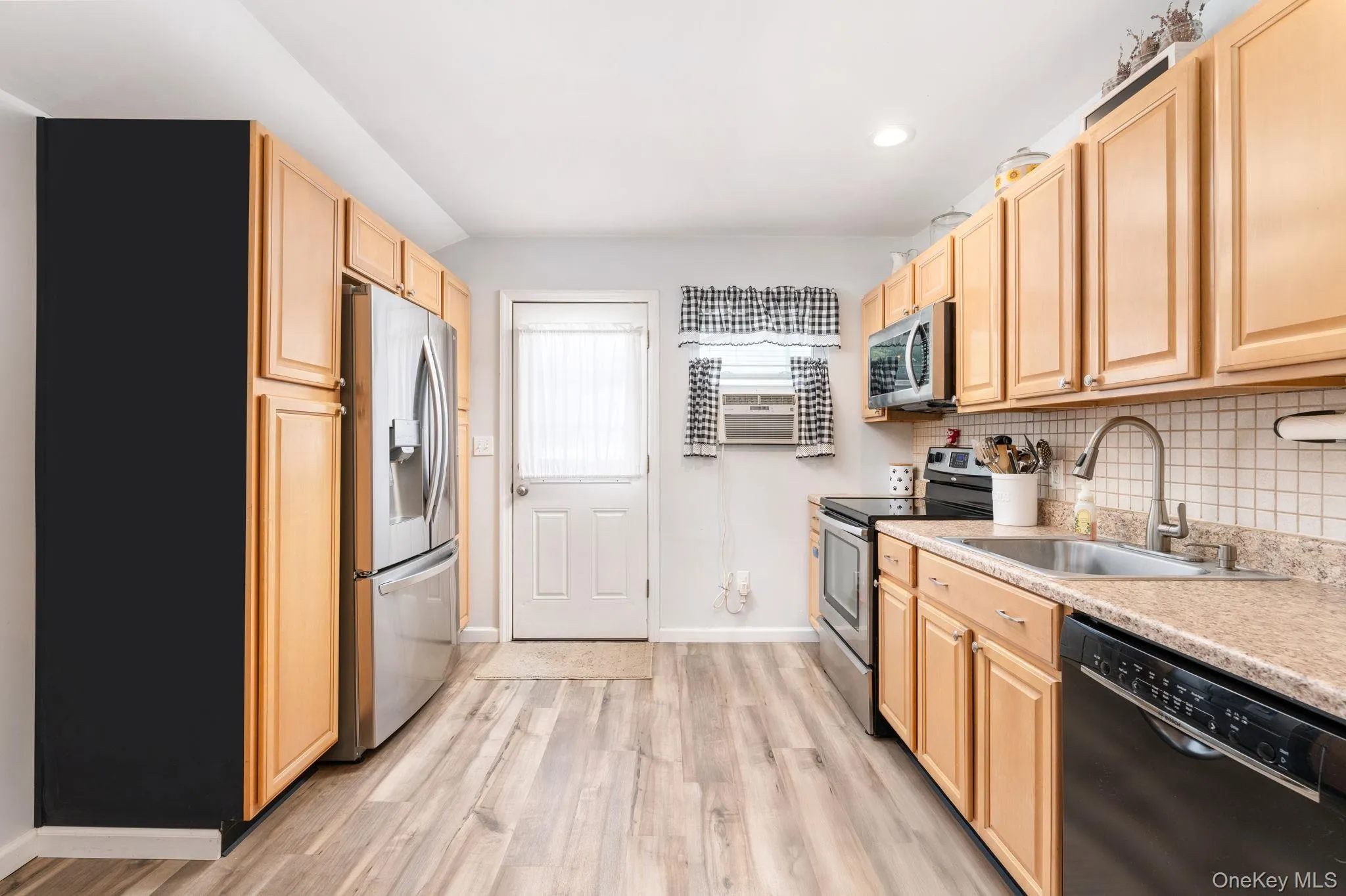 Kitchen featuring wood-finish flooring, light wood cabinetry, a stainless steel refrigerator, and a tile backsplash Kitchen featuring wood-finish flooring, light wood cabinetry, a stainless steel refrigerator, and a tile backsplash