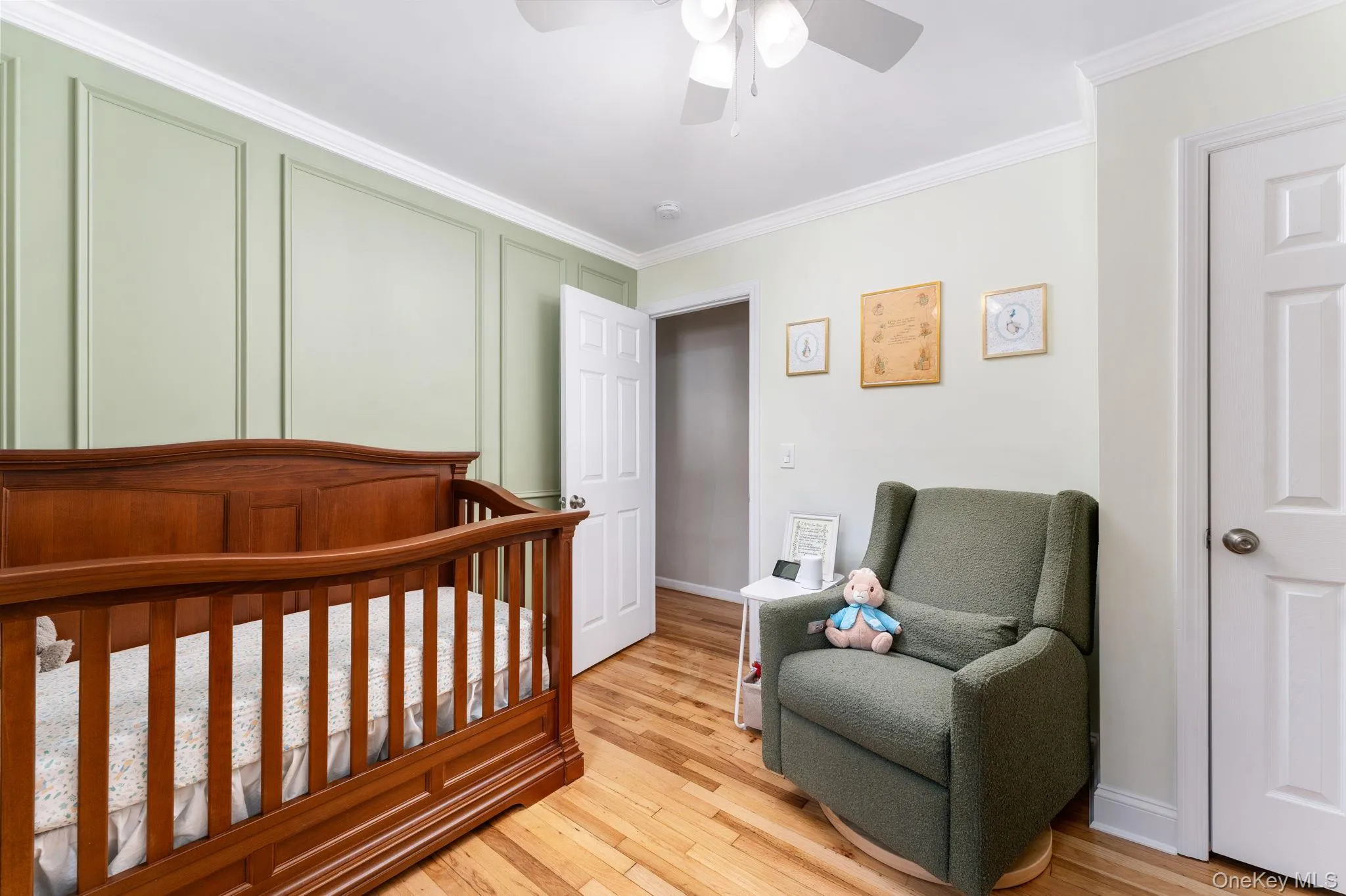 Bedroom featuring accent wall with decorative molding, ceiling fan, wood-finish flooring, and white trim Bedroom featuring accent wall with decorative molding, ceiling fan, wood-finish flooring, and white trim