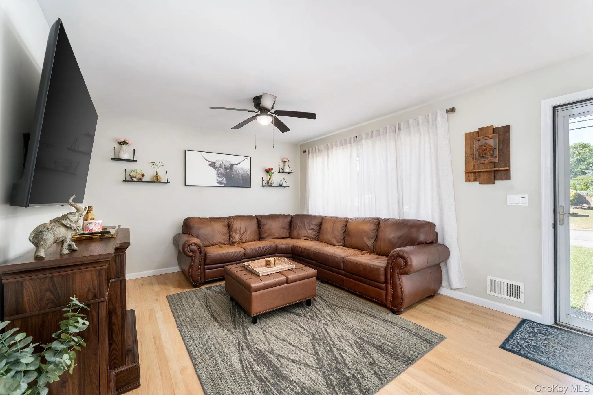Bright living space featuring light wood-finish flooring, a ceiling fan with integrated lighting, and light-toned walls Bright living space featuring light wood-finish flooring, a ceiling fan with integrated lighting, and light-toned walls