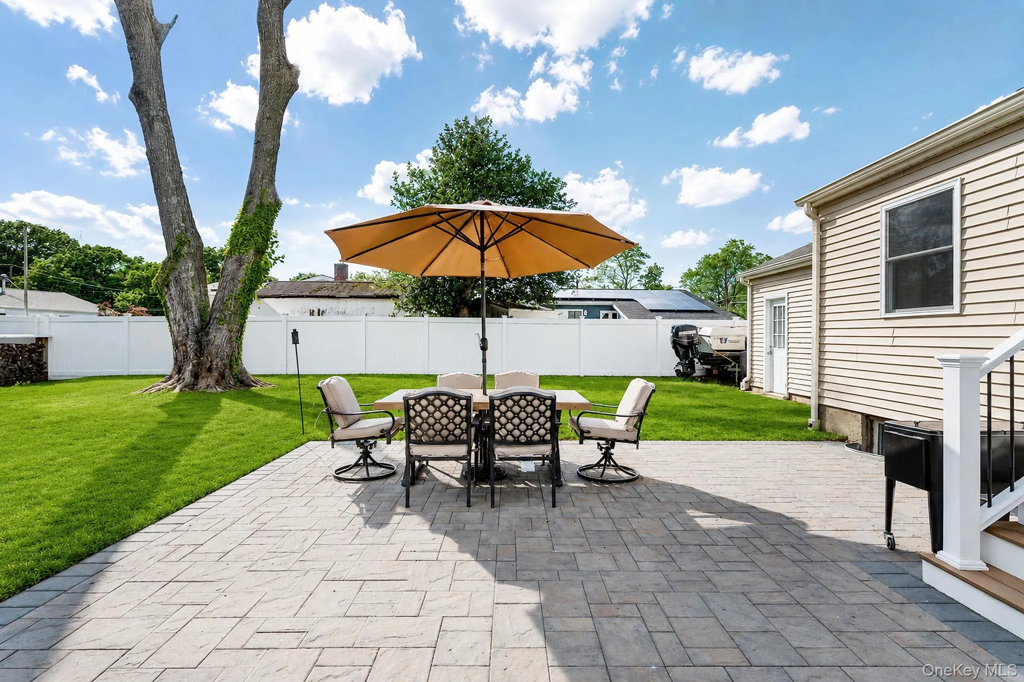 Expansive paver patio with a manicured lawn, white privacy fencing, and exterior siding Expansive paver patio with a manicured lawn, white privacy fencing, and exterior siding