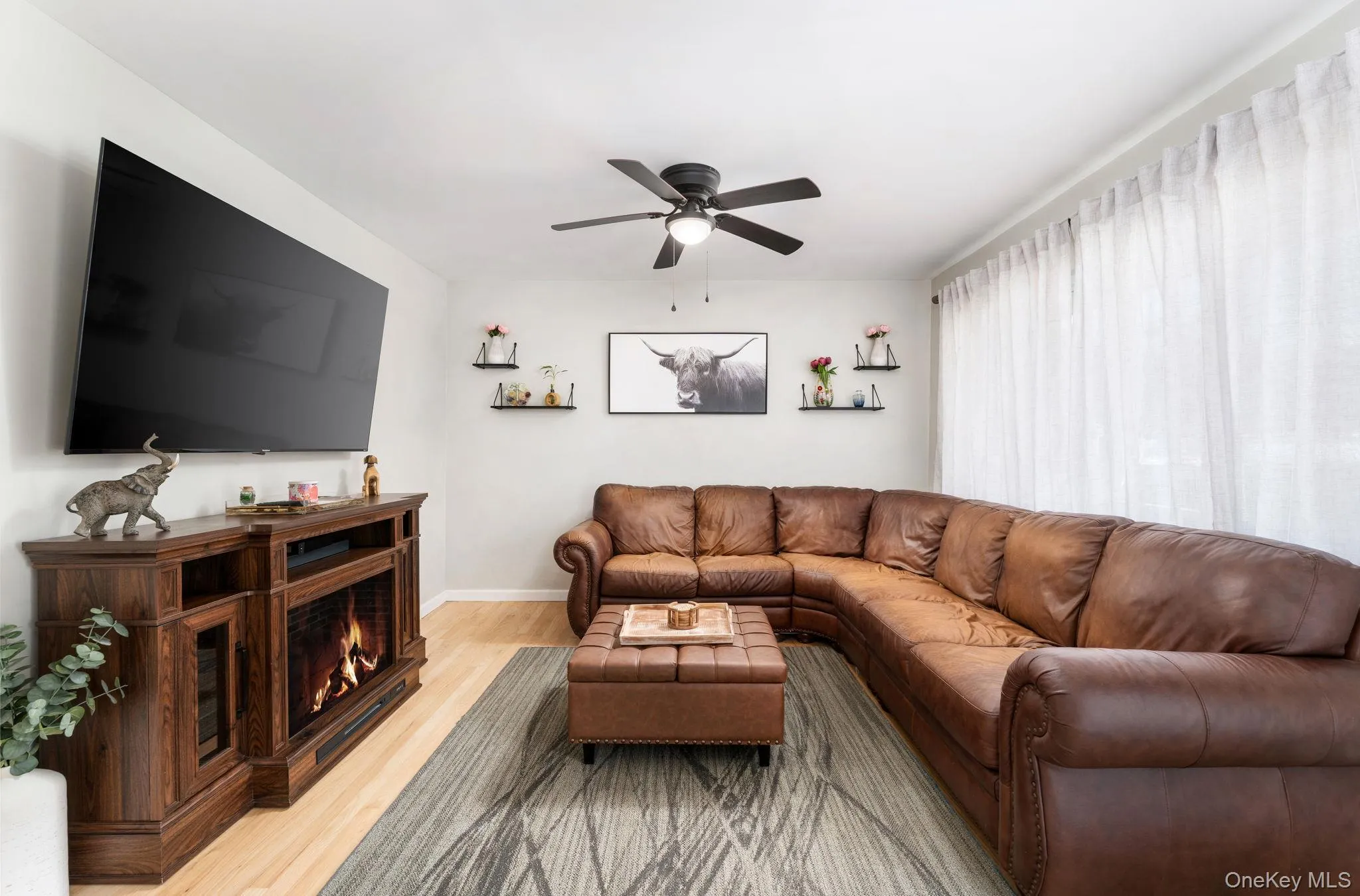 Living area featuring light wood-finish flooring and an electric fireplace within a dark wood media console Living area featuring light wood-finish flooring and an electric fireplace within a dark wood media console