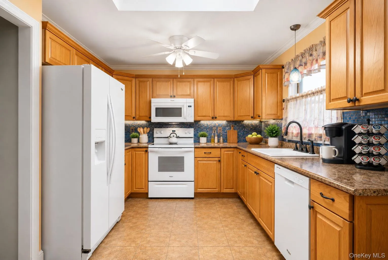 Kitchen featuring extensive wood cabinetry, white appliances, a tile backsplash, and a ceiling fan Kitchen featuring extensive wood cabinetry, white appliances, a tile backsplash, and a ceiling fan