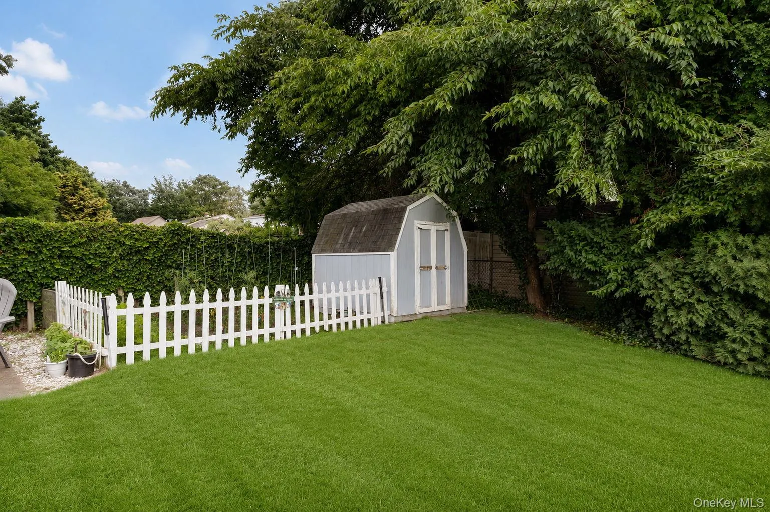 Expansive lawn area featuring a white picket fence, a garden shed with a gambrel roof, and mature perimeter trees Expansive lawn area featuring a white picket fence, a garden shed with a gambrel roof, and mature perimeter trees
