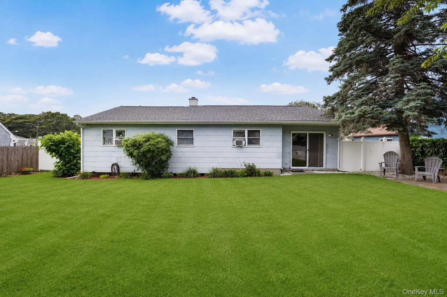 Expansive green lawn with a single-story residence featuring light-colored siding, a dark shingled roof, and a sliding glass door providing exterior access Expansive green lawn with a single-story residence featuring light-colored siding, a dark shingled roof, and a sliding glass door providing exterior access