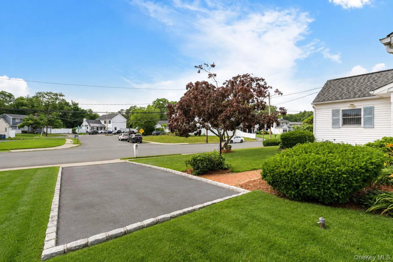 Spacious front yard featuring manicured green lawn, mature landscaping, and an asphalt driveway with Belgian block curbing Spacious front yard featuring manicured green lawn, mature landscaping, and an asphalt driveway with Belgian block curbing