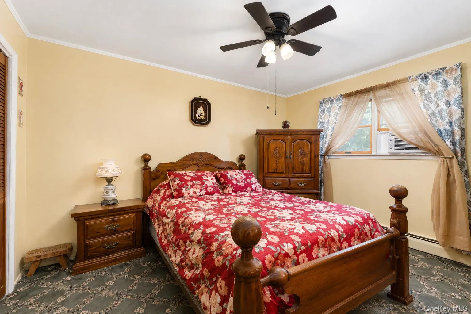Bedroom featuring soft yellow walls, patterned carpet, a ceiling fan with integrated lighting, and a window with a window-mounted air conditioning unit Bedroom featuring soft yellow walls, patterned carpet, a ceiling fan with integrated lighting, and a window with a window-mounted air conditioning unit