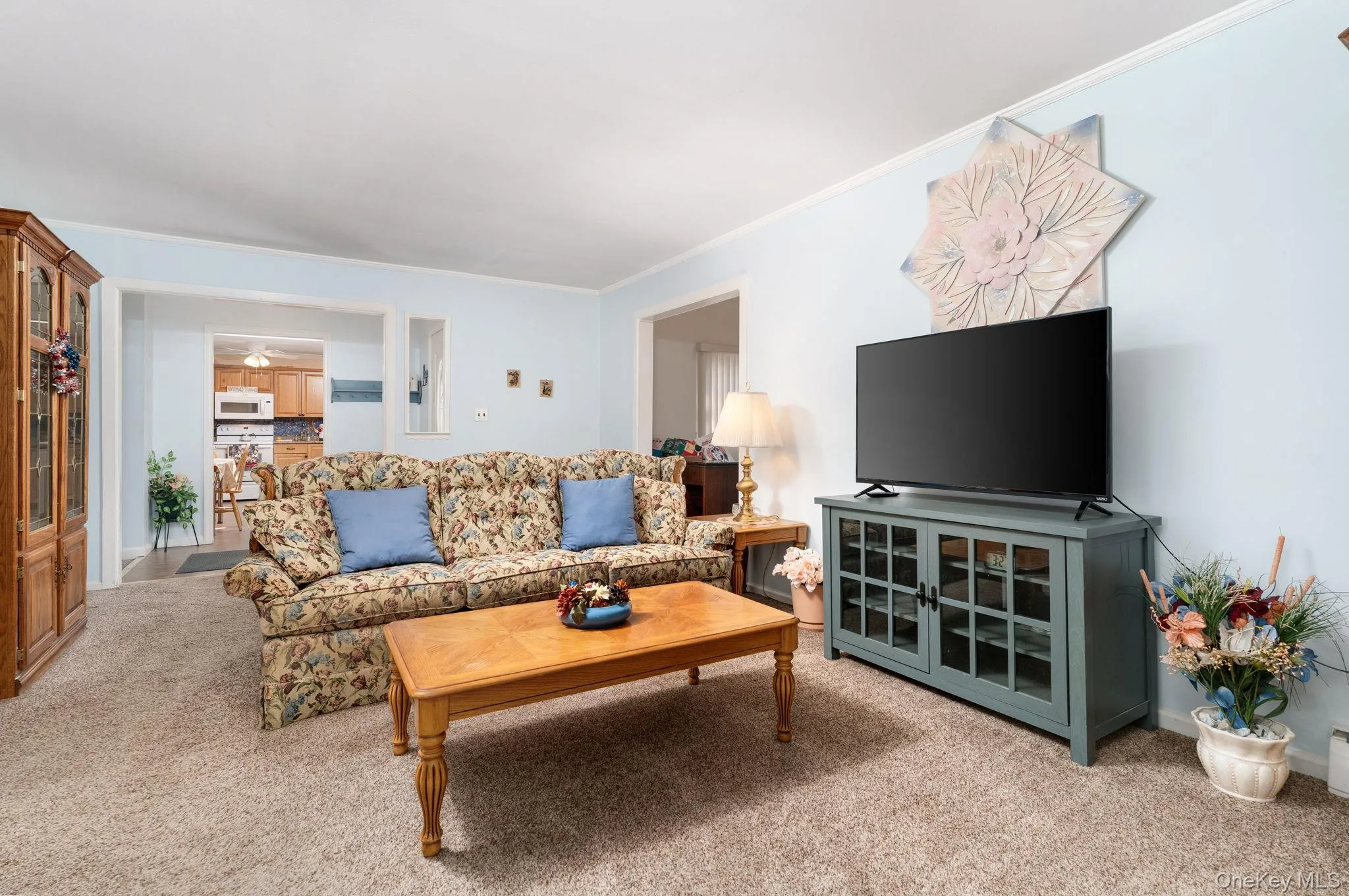 Living area featuring light blue walls, neutral carpet flooring, and white crown molding Living area featuring light blue walls, neutral carpet flooring, and white crown molding